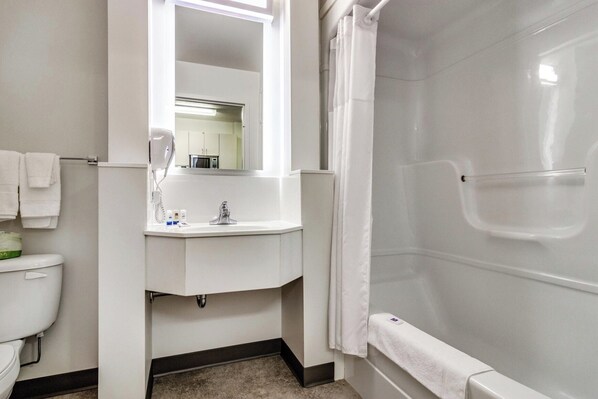 A bathroom with a toilet, sink, mirror, and shower. - Motel 6 Saskatoon, SK (Saskatoon)