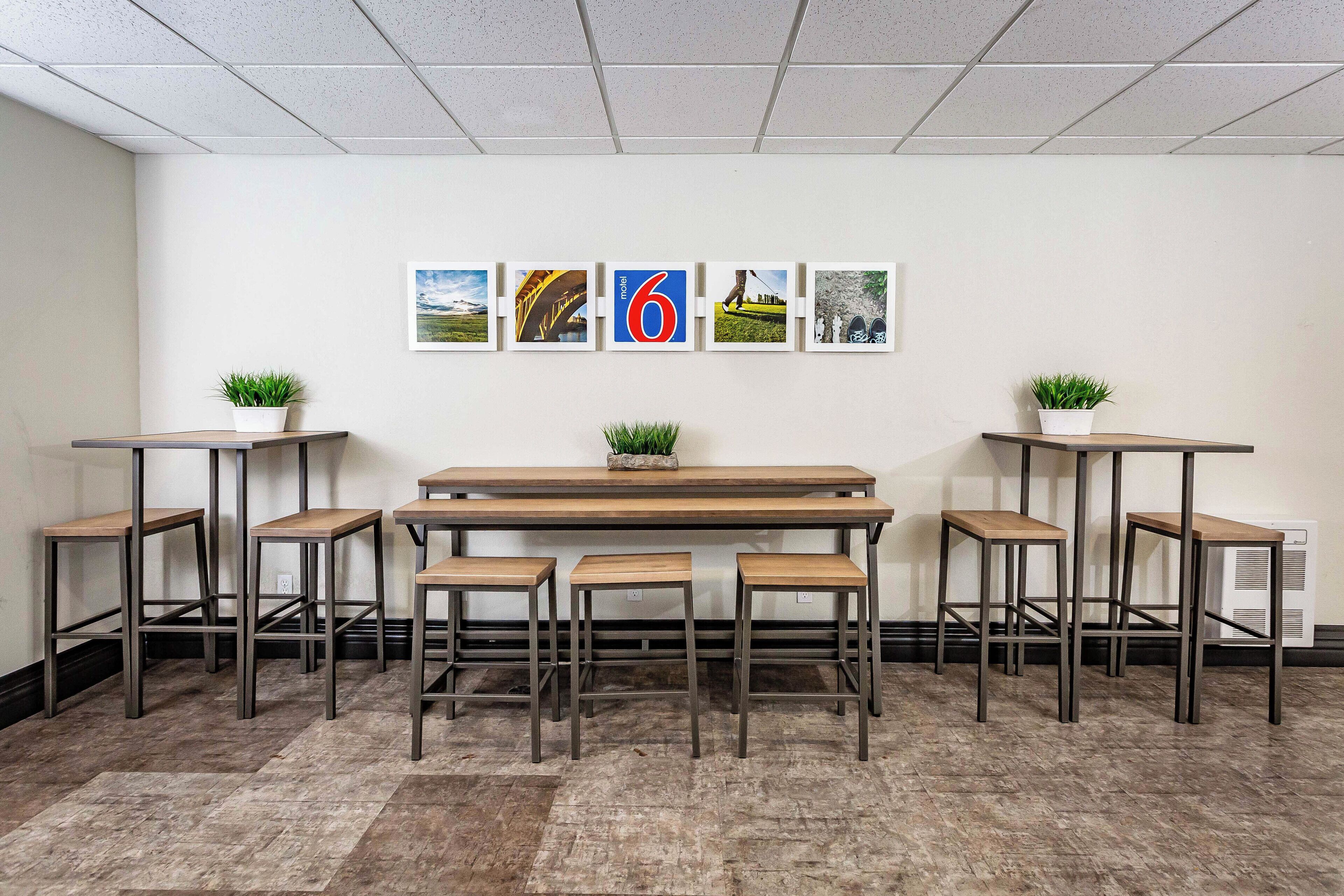 A modern interior with a long table and six stools, a ceiling with grid lights, and four framed pictures on the wall.