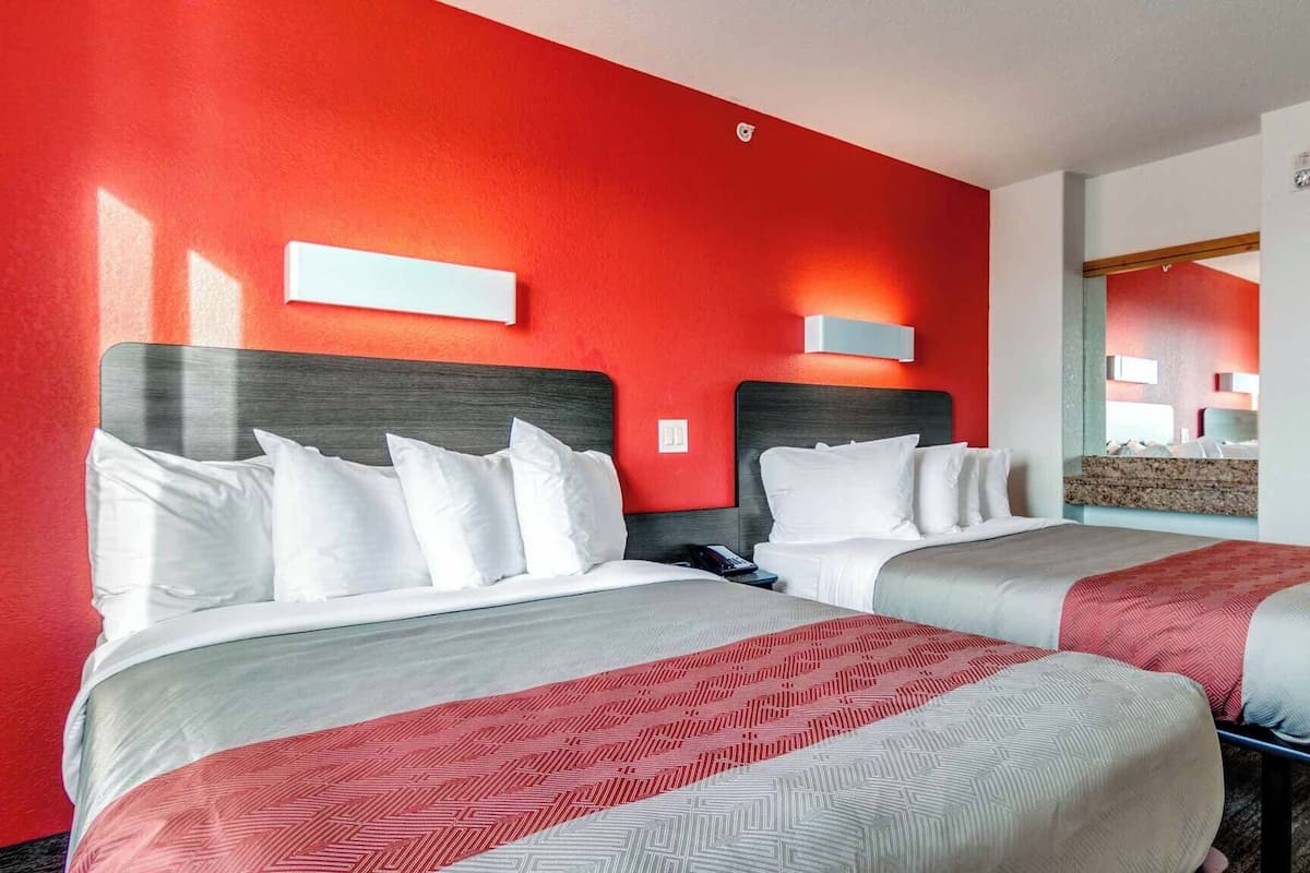 Quarto de hotel com duas camas, paredes vermelhas e um espelho.