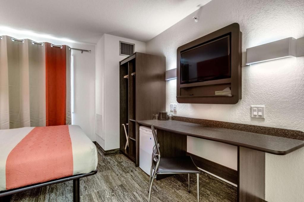 Une chambre d’hôtel équipée d’un lit, d’un bureau, d’une chaise, d’une télévision et d’un petit réfrigérateur.