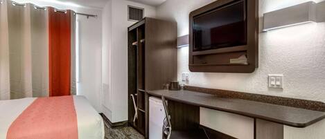 Ein Hotelzimmer mit Bett, Schreibtisch, Stuhl, Fernseher und kleinem Kühlschrank.