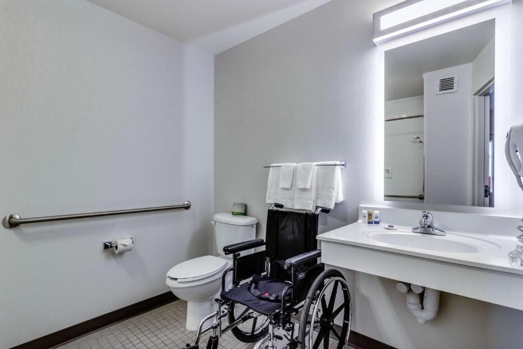 A wheelchair-accessible bathroom with a toilet, sink, and handrails.