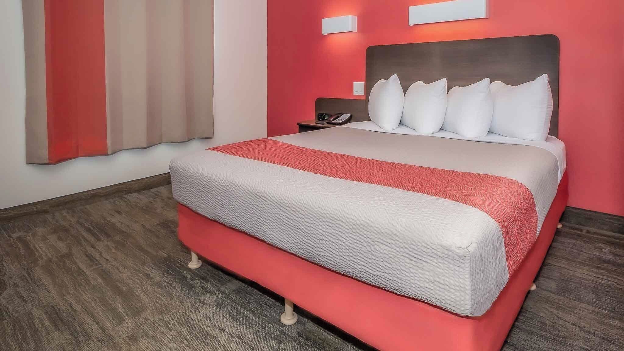 A hotel room with a bed, a nightstand, a telephone, and a wall-mounted light.
