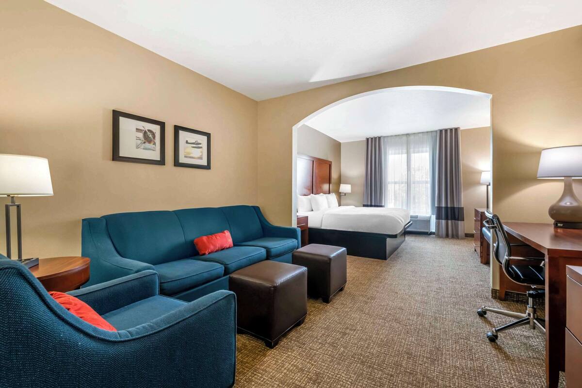 A hotel room with a blue sofa, a bed, a desk, and a chair.