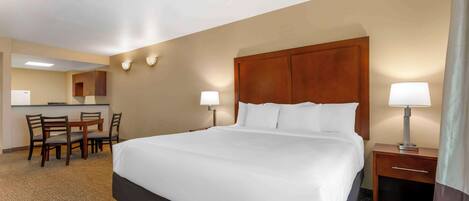 A hotel room with a large bed, a desk with a chair, a small table, and a lamp.