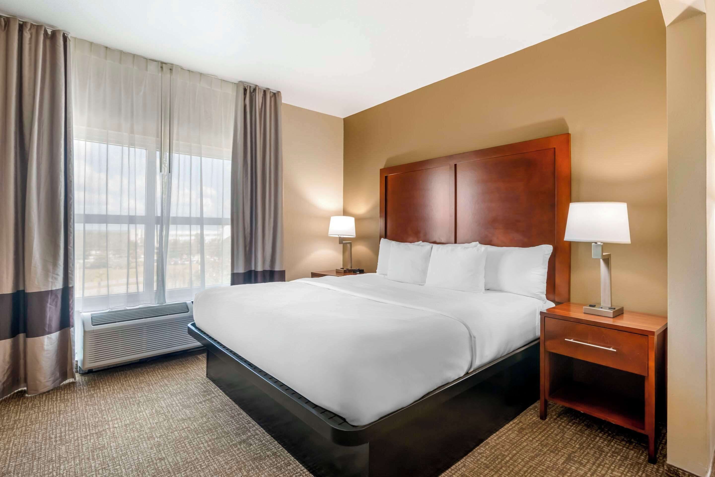 Une chambre d’hôtel avec un grand lit, deux tables de chevet avec des lampes, une fenêtre avec des rideaux et un climatiseur fixé au mur.