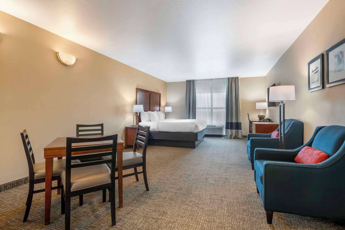 A hotel room with a bed, a desk with chairs, a sofa, and a lamp.