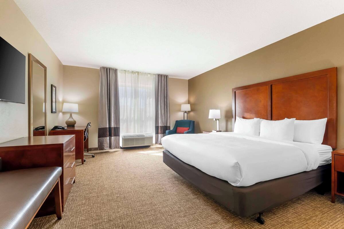 A hotel room with a large bed, a desk, a chair, a TV, and a window with curtains.