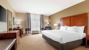 A hotel room with a large bed, a desk, a chair, a TV, and a window with curtains.