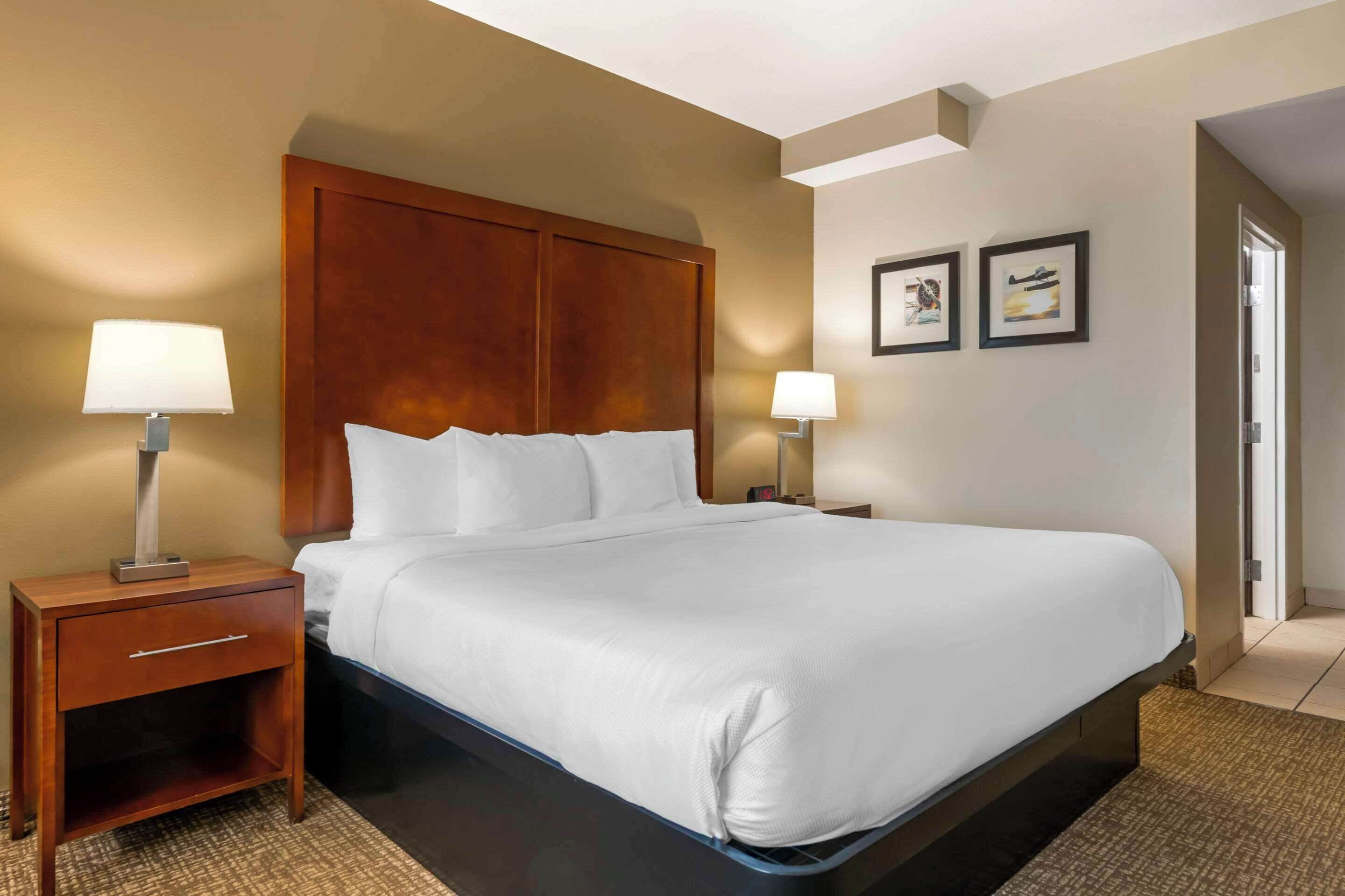 A hotel room with a large bed, two bedside tables with lamps, a wooden headboard, and two framed pictures on the wall.