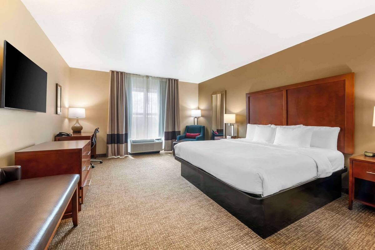 A hotel room with a large bed, a desk, a chair, a TV, and a window with curtains.