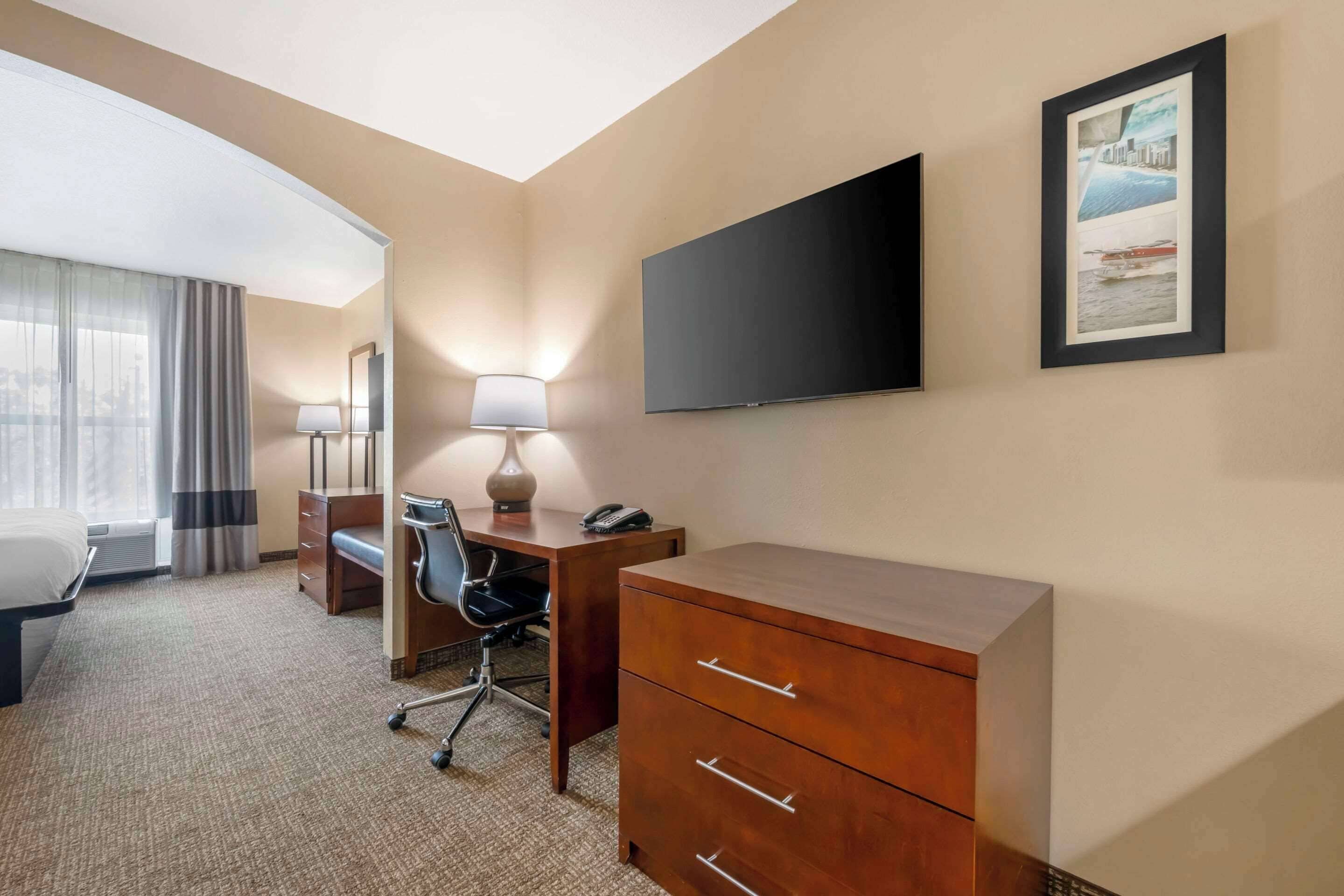 Een hotelkamer met een bed, bureau, stoel, lamp, televisie en een lijstje aan de muur.
