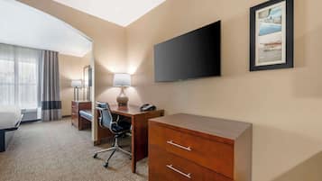 A hotel room with a bed, desk, chair, lamp, TV, and a framed picture on the wall.