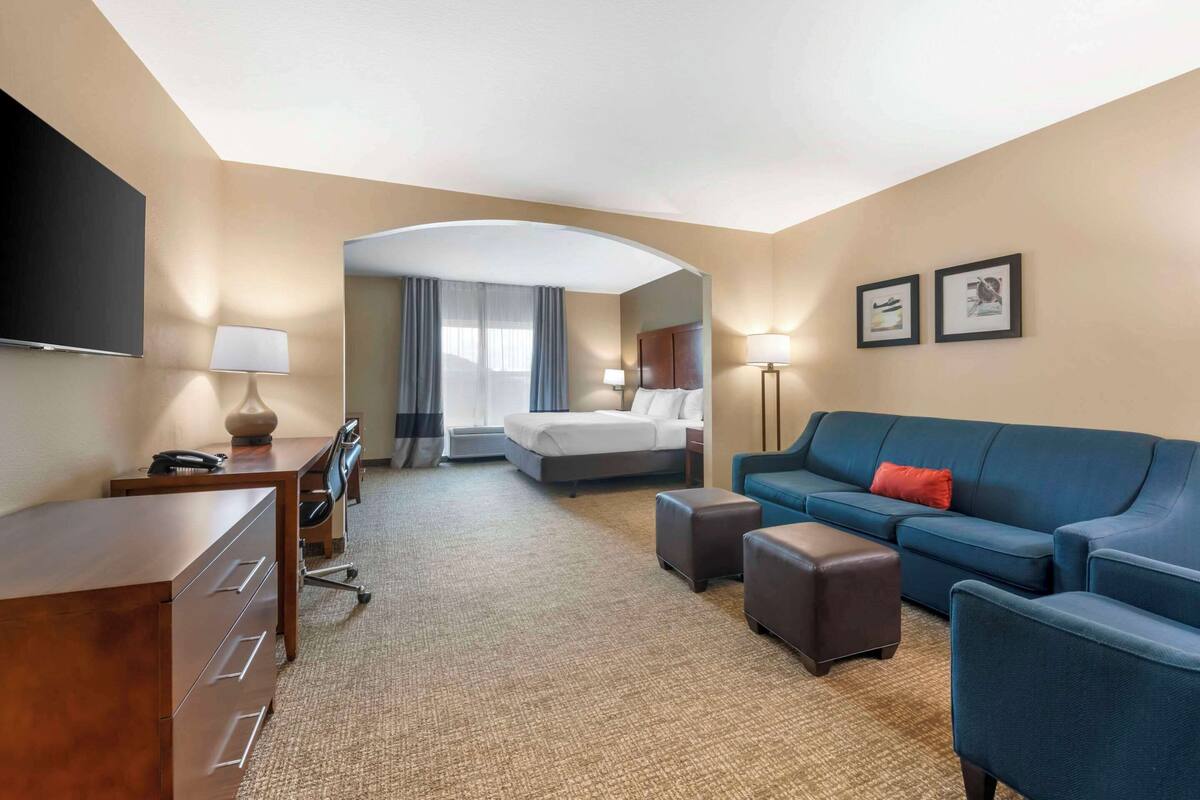 A hotel room with a bed, a desk with a lamp, a sofa, and a TV mounted on the wall.