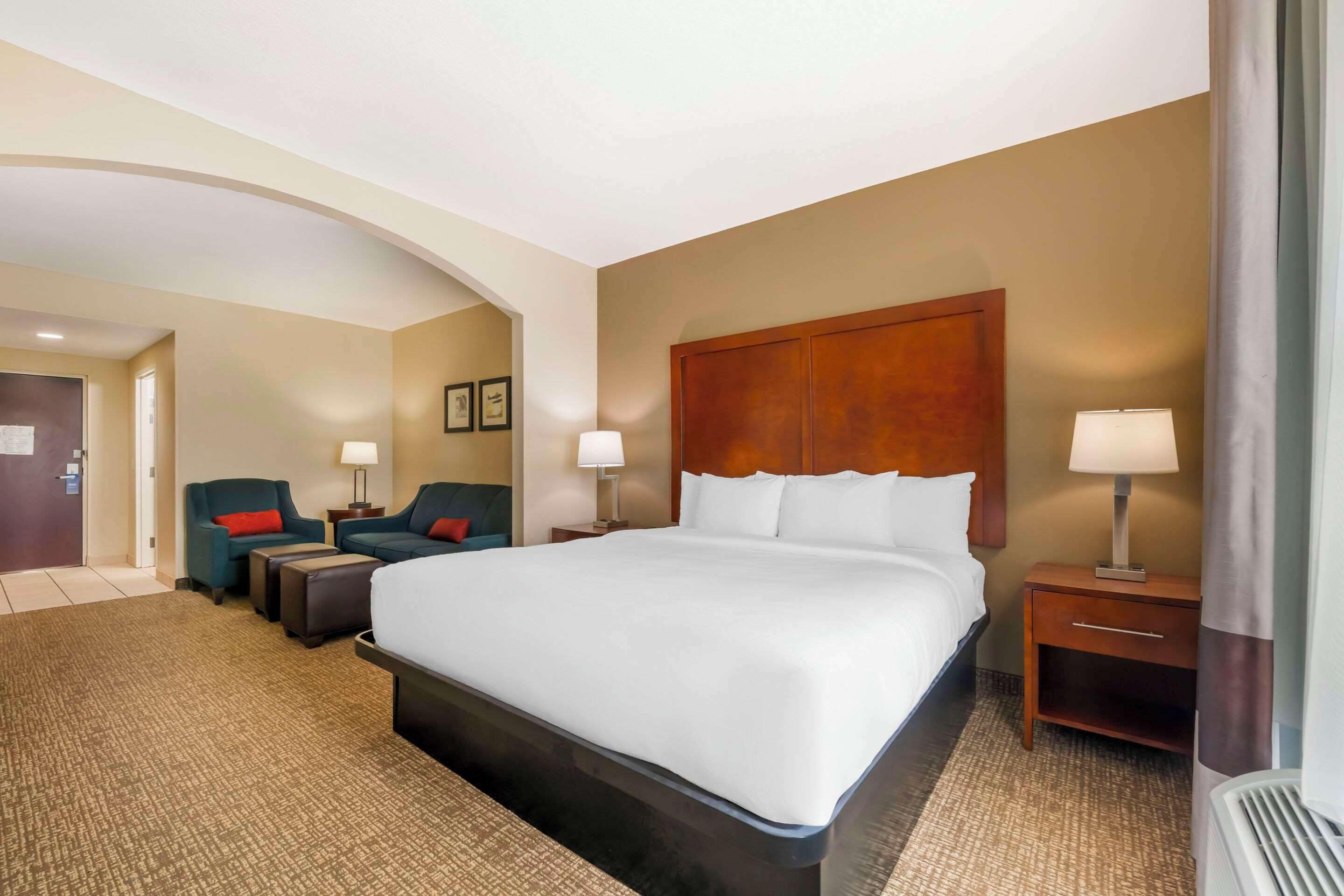 Una habitación de hotel con una cama grande, dos mesitas de noche con lámparas, un sofá y una silla.