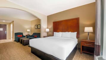 A hotel room with a large bed, two bedside tables with lamps, a sofa, and a chair.