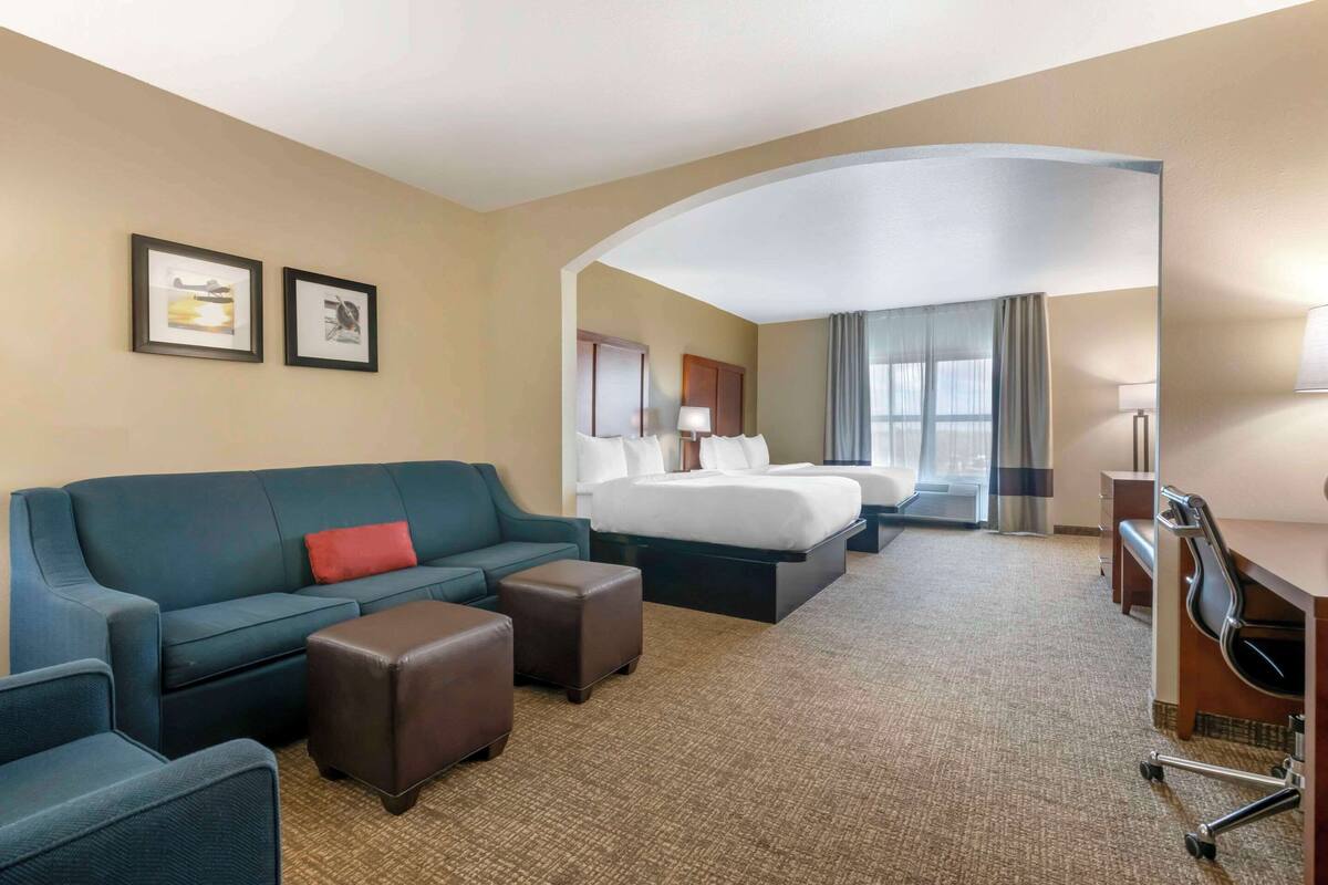 A hotel room with a sofa, two ottomans, a desk, a bed, and a TV.