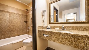 Un baño con bañera, inodoro, encimera de granito, lavabo, espejo y ducha.