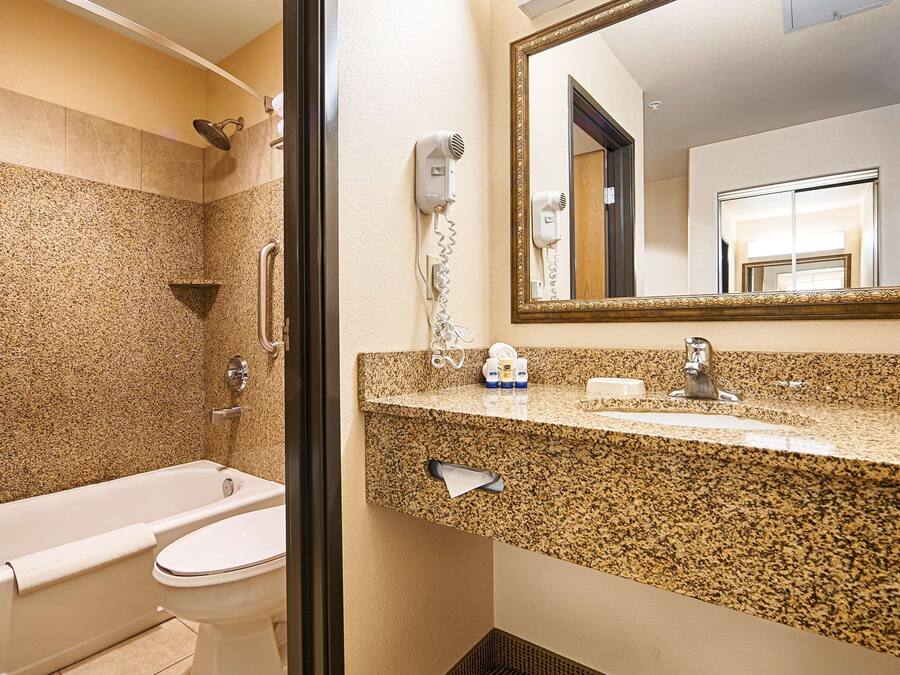 Ein Badezimmer mit Badewanne, Toilette, einer Arbeitsplatte aus Granit, Waschbecken, Spiegel und Duschkopf.