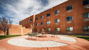 Un edificio moderno con un patio que incluye una fuente, asientos y un césped cuidado.