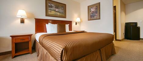 Habitación de hotel con una cama grande, dos lámparas de noche, una mesita de noche, un refrigerador y dos cuadros en la pared.