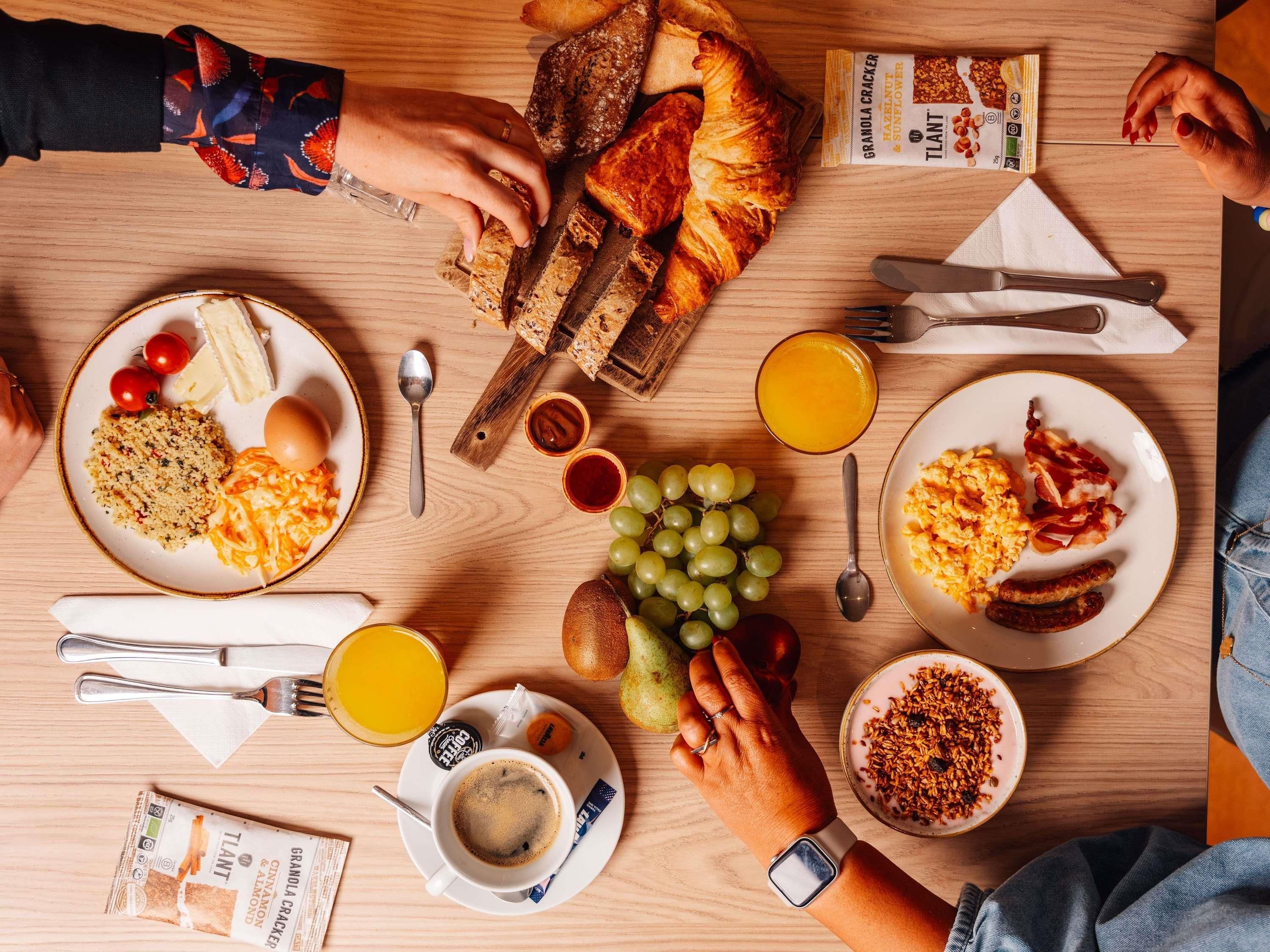 A breakfast setting with various food items and utensils on a wooden table.