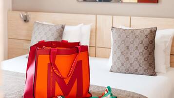 Een hotelkamer met een bed, kussens, een deken, een grote oranje tas en een kleurrijke sjaal.