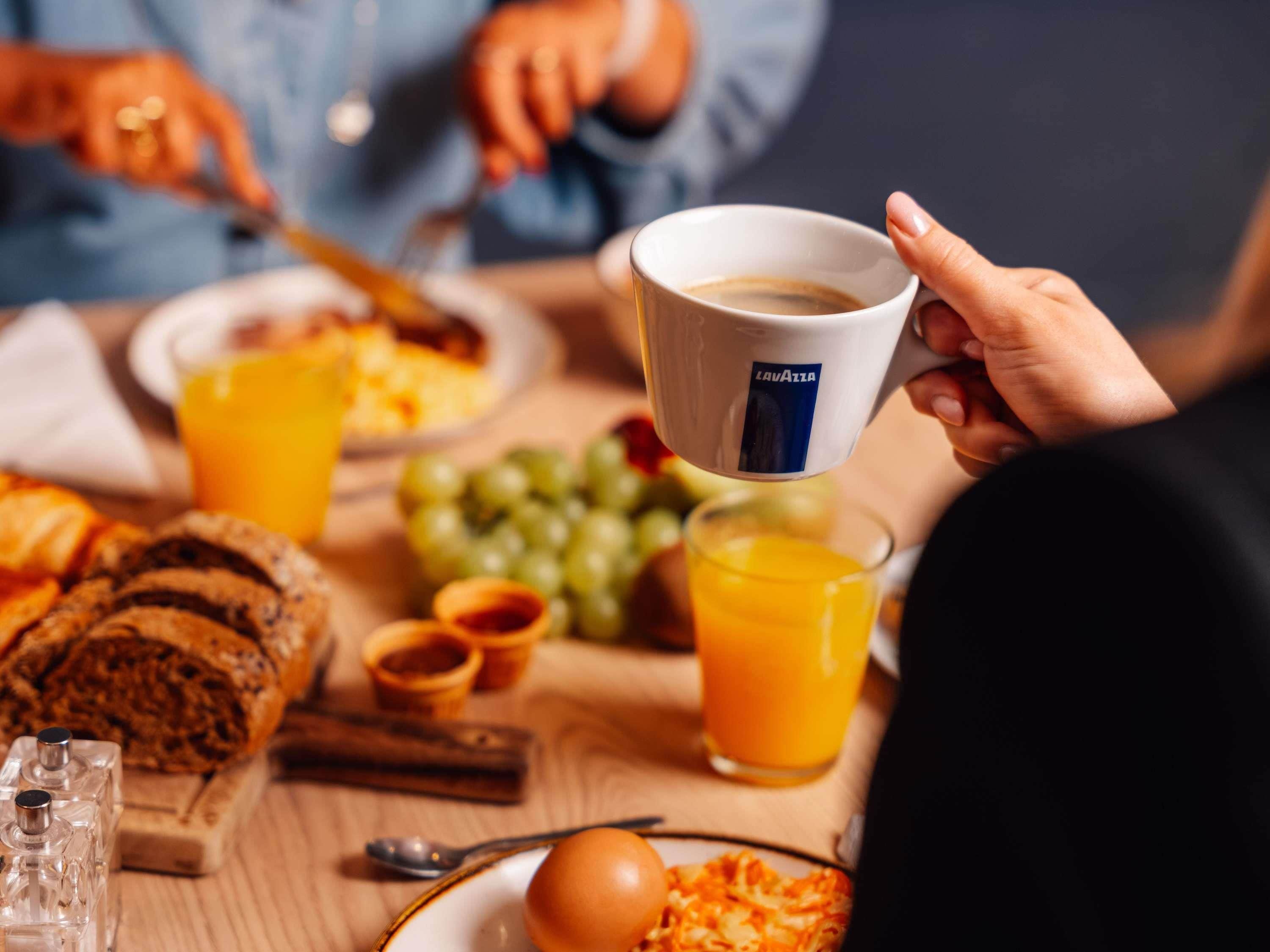 A breakfast setting with a cup of coffee, orange juice, and various breakfast items on a table.