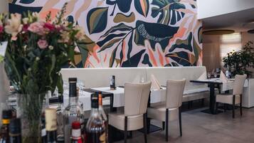 A restaurant interior with a modern design, featuring a large abstract mural on the wall, a seating area with tables and chairs, and a vase with flowers on the table.