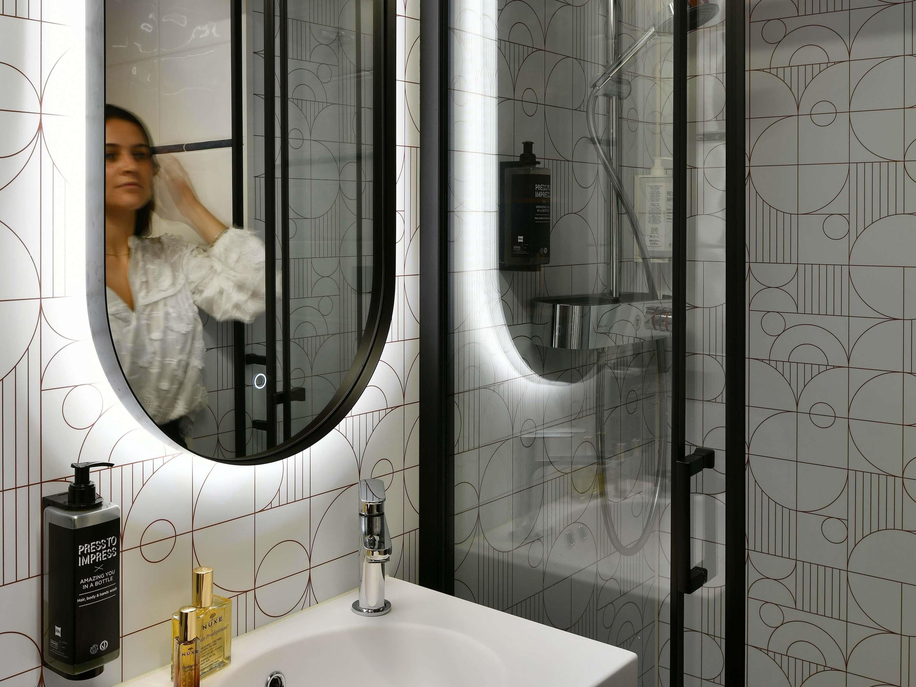 Een badkamer met een ronde spiegel, een wastafel, een douche en een fles haarproduct.