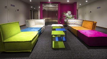 Un área de espera moderna con asientos coloridos, una pequeña mesa y un ascensor al fondo.
