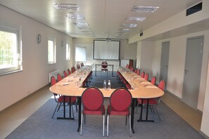 A conference room with a long table, red chairs, a projector screen, and a whiteboard. - Ibis Styles Charleroi Airport Aero44 (Charleroi)