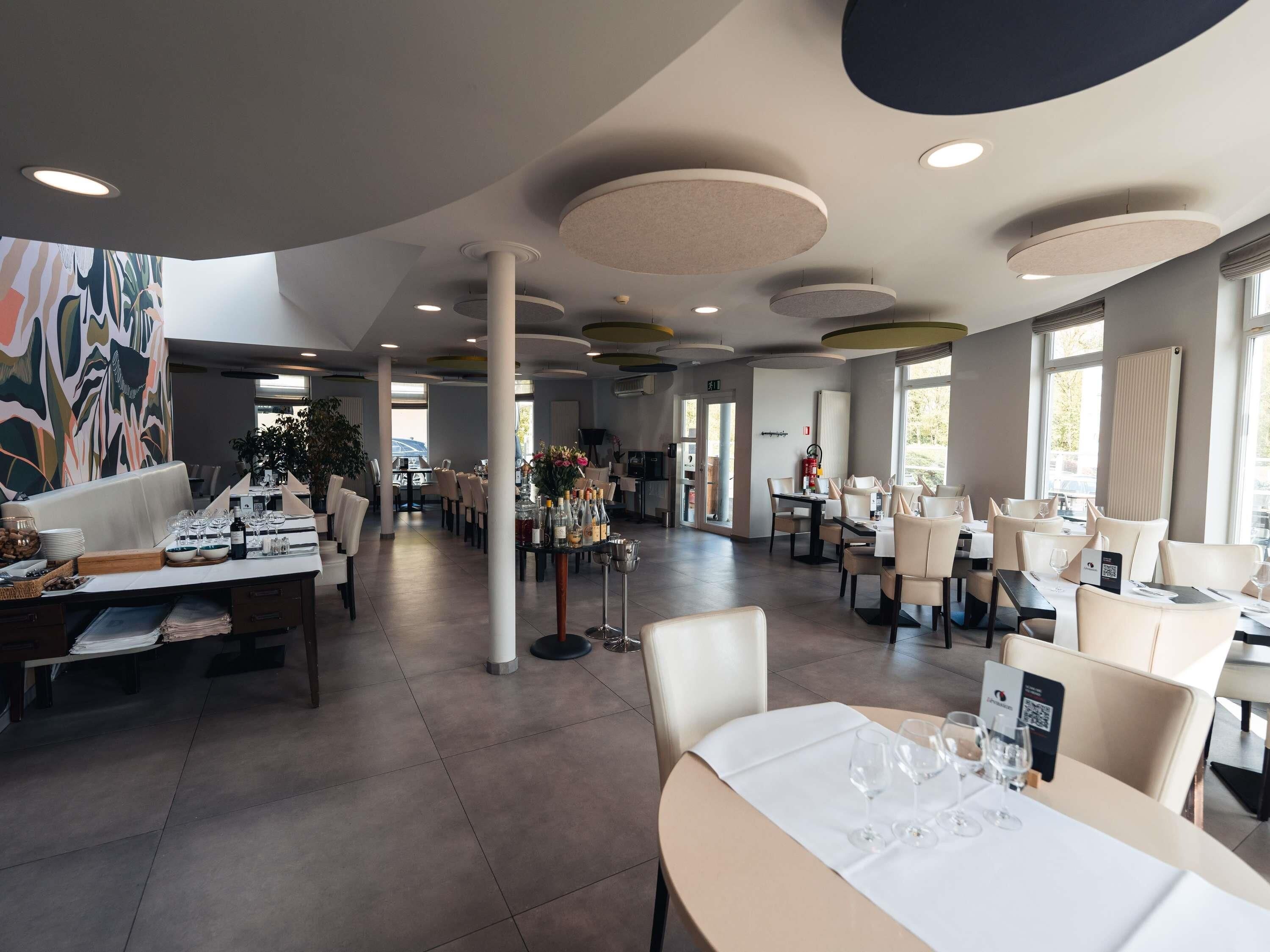 Ein geräumiger Hotel-Speisesaal mit mehreren Tischen und Stühlen, einer zentralen Blumenkomposition und einem modernen Deckenbau.