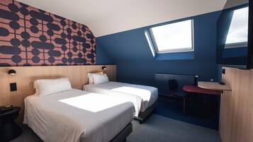 A hotel room with two beds, a desk, a chair, a radiator, and a large window.