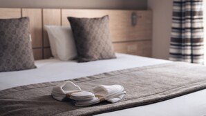 Una cama bien tendida con un edredón gris y un par de pantuflas blancas.