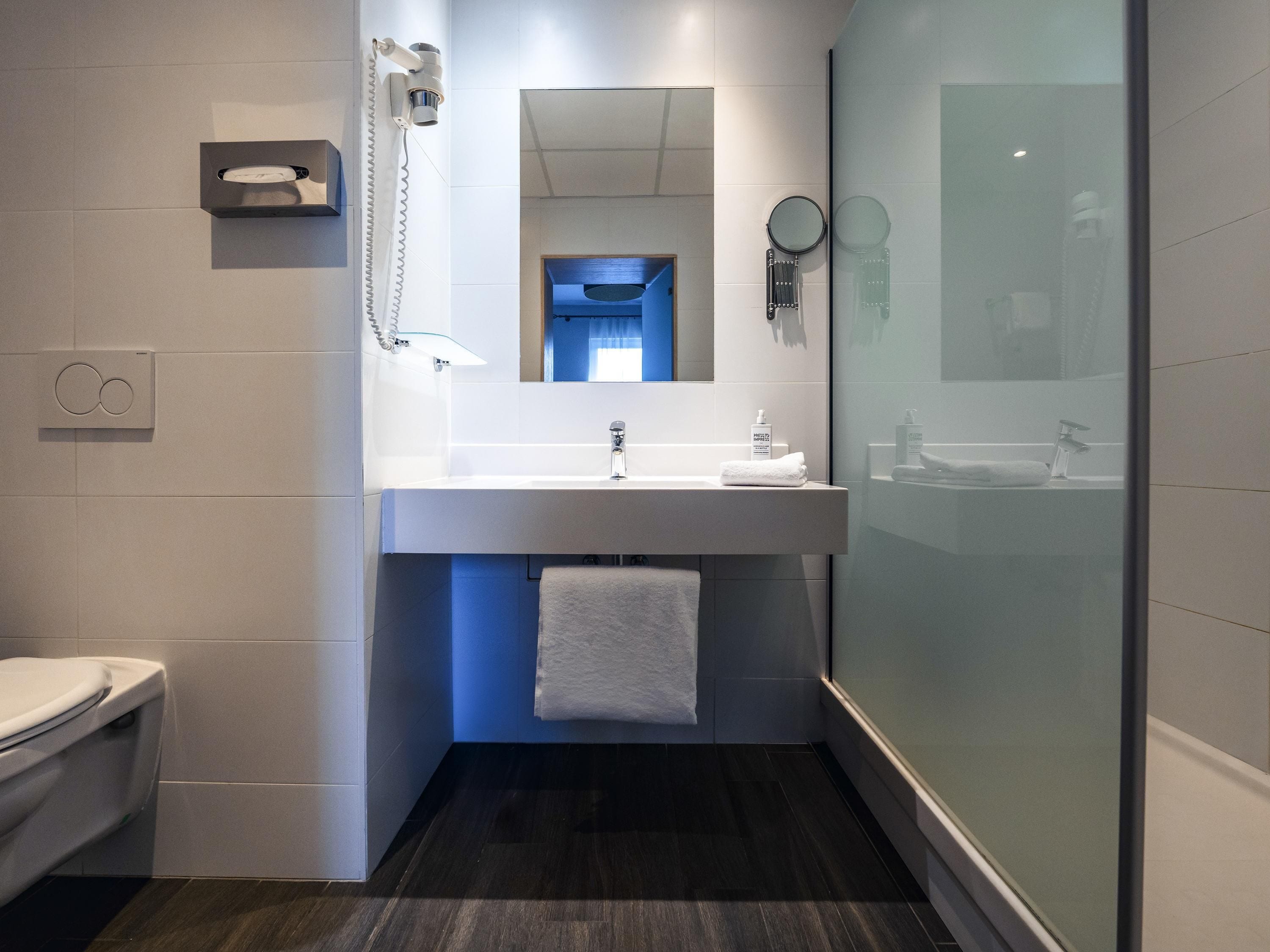 A modern bathroom with a white sink, a mirror, a towel, and a shower area.