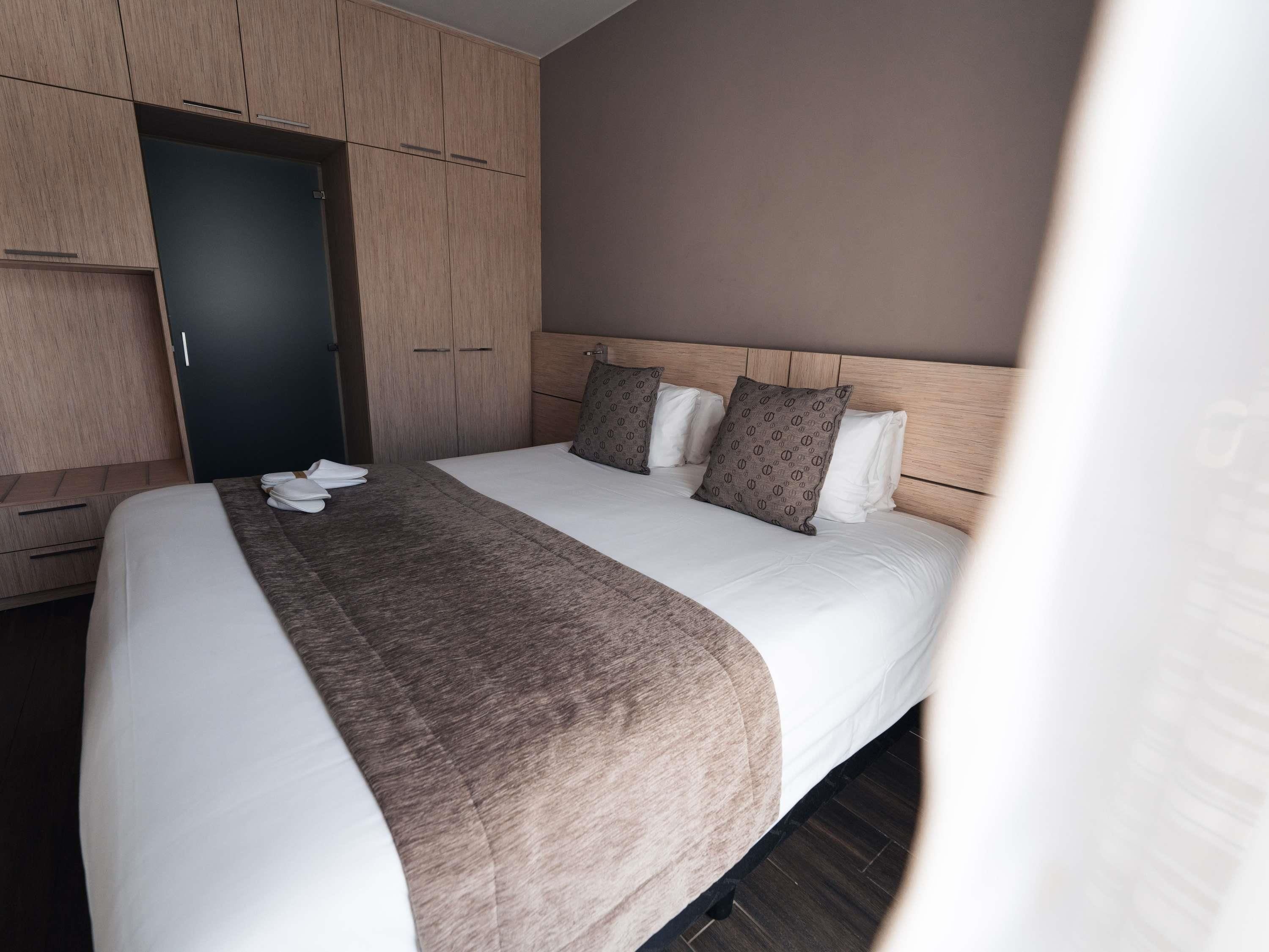 A hotel room with a large bed, a wardrobe, and a door.