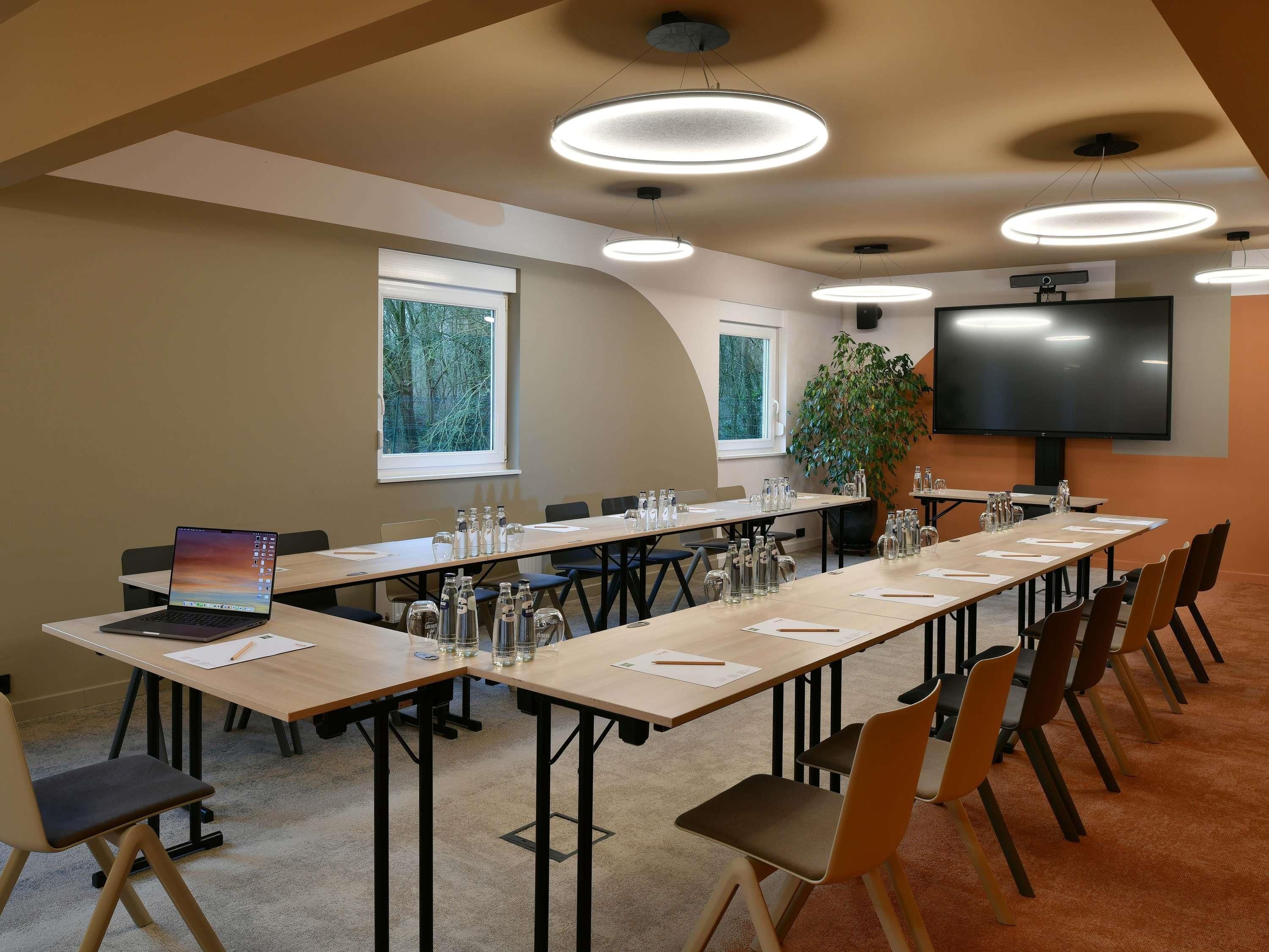 A conference room with a long table, chairs, a laptop, water bottles, and a TV screen.