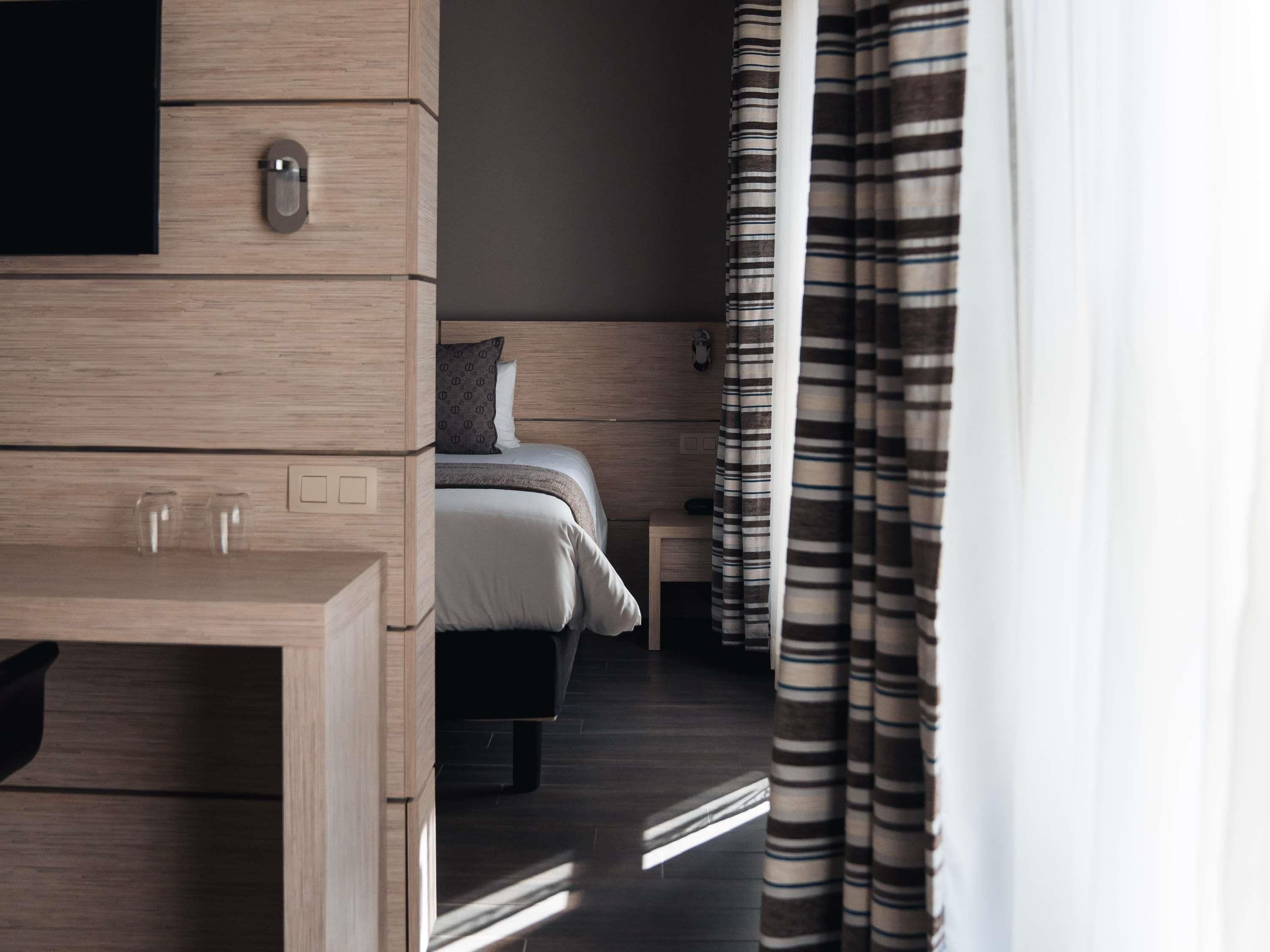 A hotel room with a bed, bedside table, and a television on a wooden dresser.