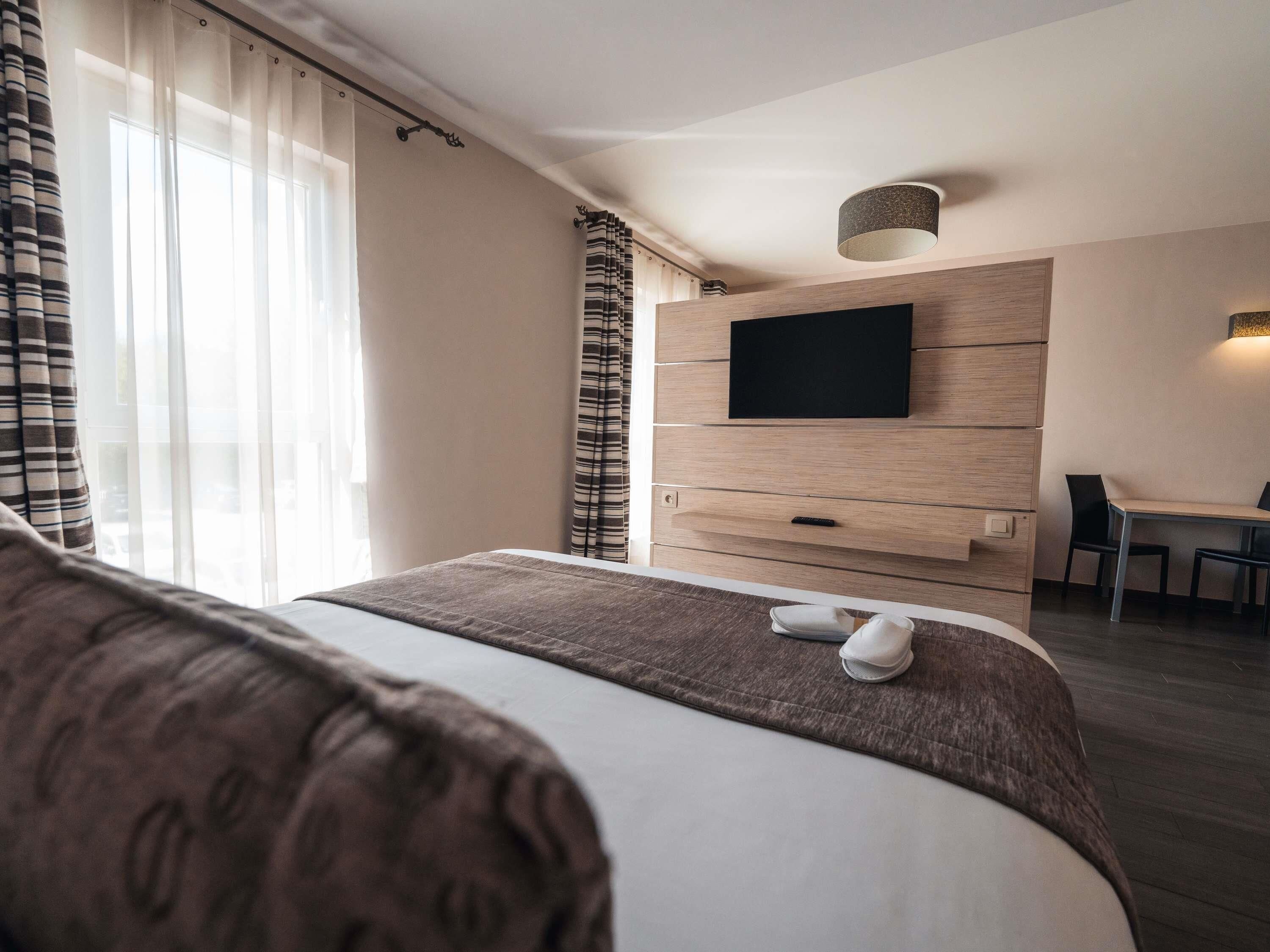 A hotel room with a bed, a TV mounted on the wall, a desk, and a chair.