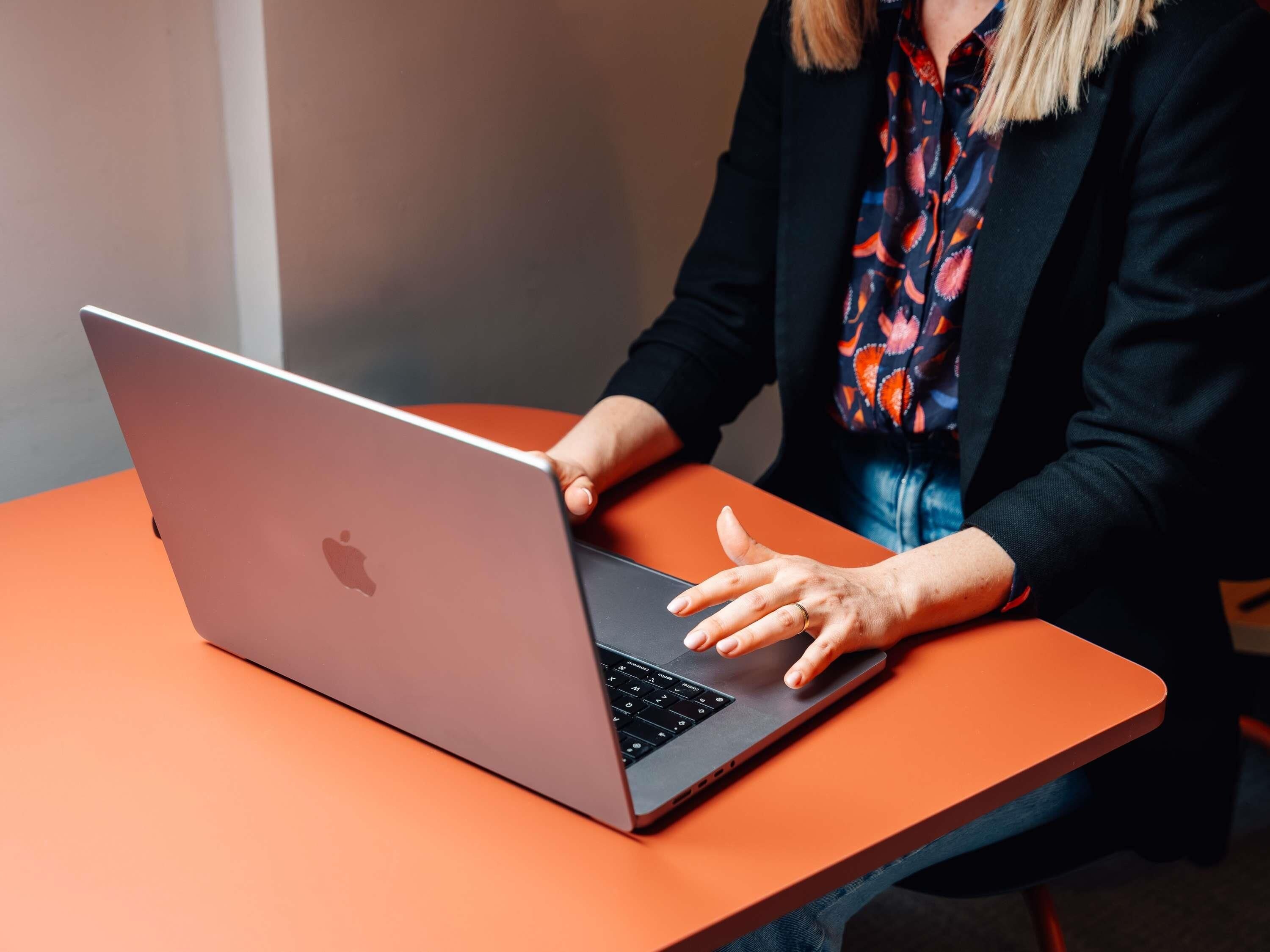 A person using a laptop on an orange table.