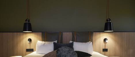A modern bedroom with a wooden headboard, two bedside lamps, and a variety of pillows.