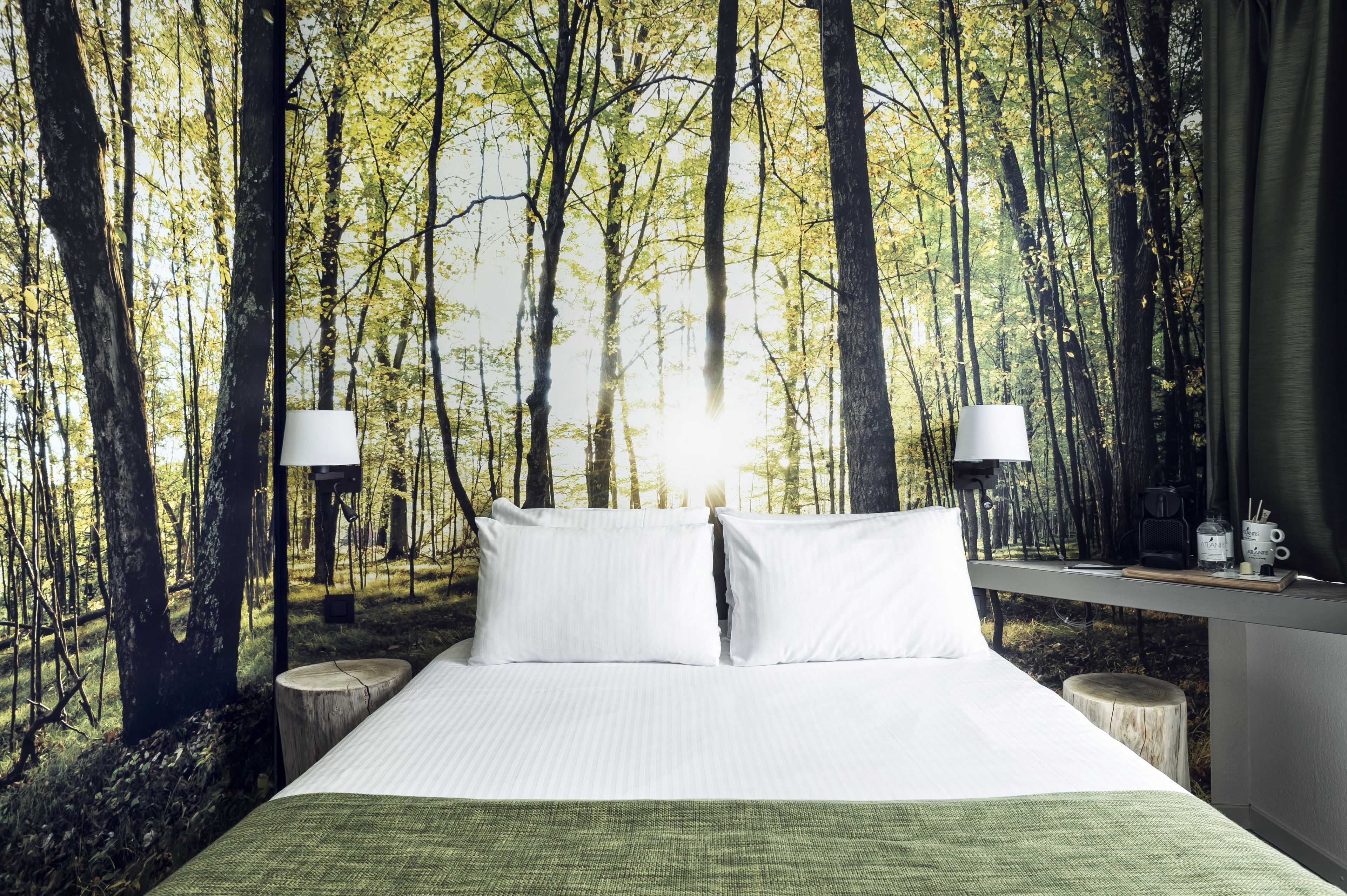 Une chambre à coucher avec un lit, deux lampes de chevet, une table de nuit et une vue sur une forêt, visible par la fenêtre.