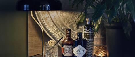 Zona de bar con un vaso, botellas de ginebra Hendrick's y whisky escocés Bobby's, frente a un fondo con diseño.