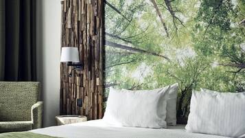 Een hotelkamer met een bed, een groene fauteuil met een patroon, een wandlamp en een groot muurschildering met een bosmotief.