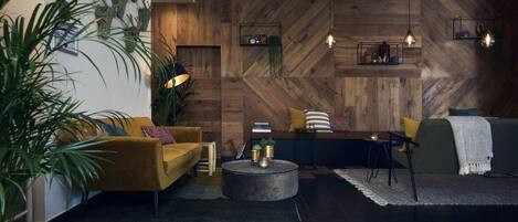Un moderno salón con una pared de madera en patrón de espiga, un sofá amarillo, un sofá verde, una mesa de centro redonda e iluminación colgante.