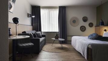 A modern, well-lit room with a sofa, a small round table, a bed, and a desk.