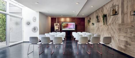 Un salón de conferencias con una pantalla grande, sillas blancas y una pared de madera.
