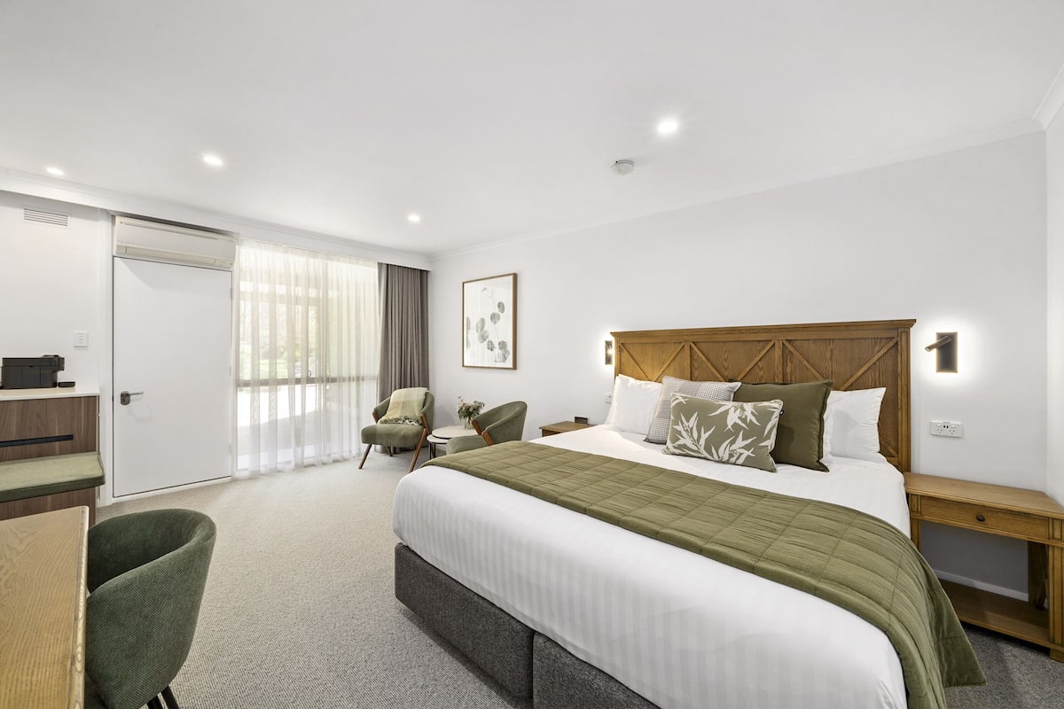 A hotel room with a large bed, a desk, a chair, a wardrobe, and a window with curtains.