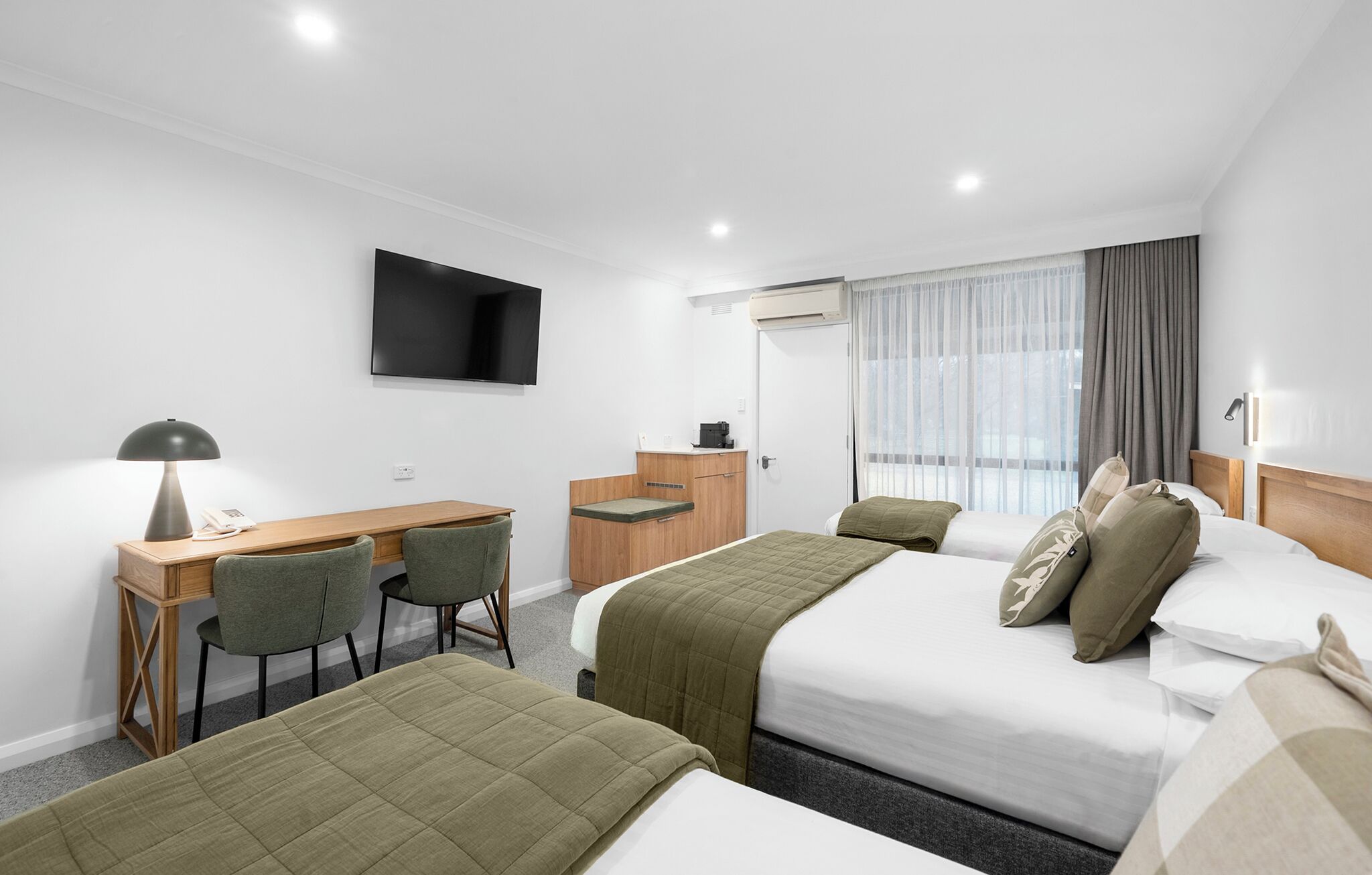 A hotel room with two beds, a desk, a chair, a TV, and a window with curtains.